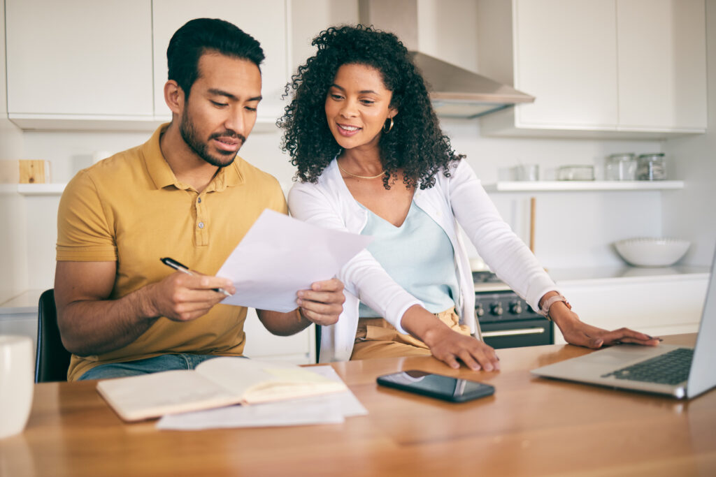 Couple reviewing a pre-approval letter at a kitchen table, planning their buy and offer strategy before touring homes
