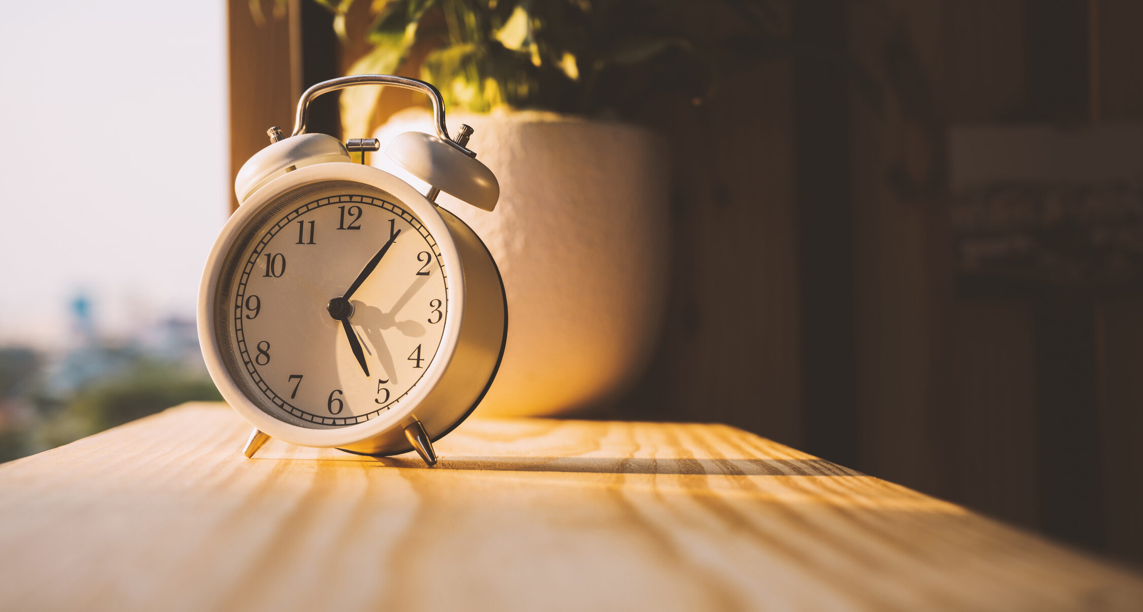 Vintage alarm clock on a window sill with flowers. Time concept.